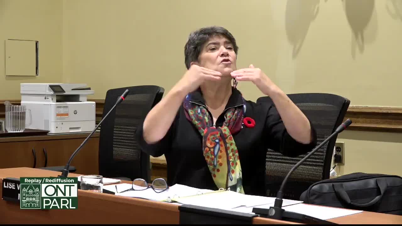 The woman gestures with both hands, her arms extended, as she speaks into the microphone at the Legislative Assembly of Ontario. She wears a colorful scarf and a poppy pin, a clear indication of the setting's formality.
The woman gestures with both hands, her arms extended, as she speaks into the microphone at the Legislative Assembly of Ontario. She wears a colorful scarf and a poppy pin, a clear indication of the setting's formality.