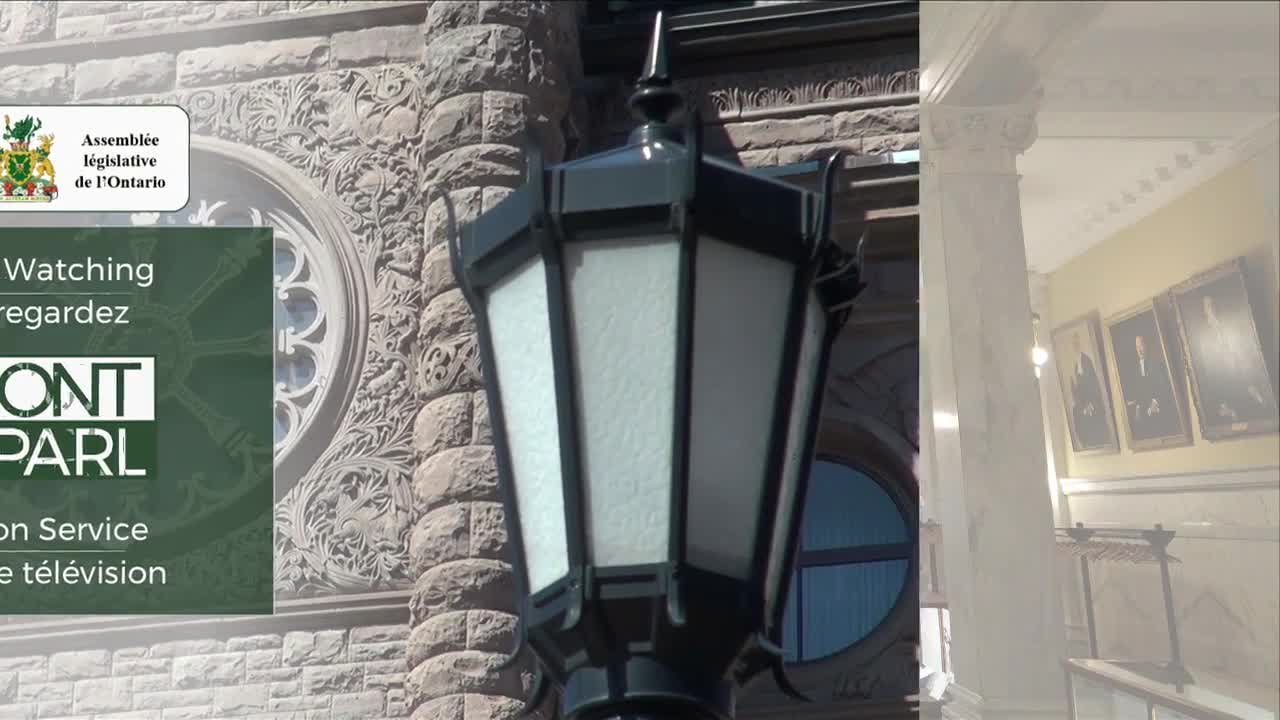 A black lamppost stands in front of the Ontario Legislative Assembly building. The ornate stonework of the building and the "ONT PARL" logo for the television service are visible.
