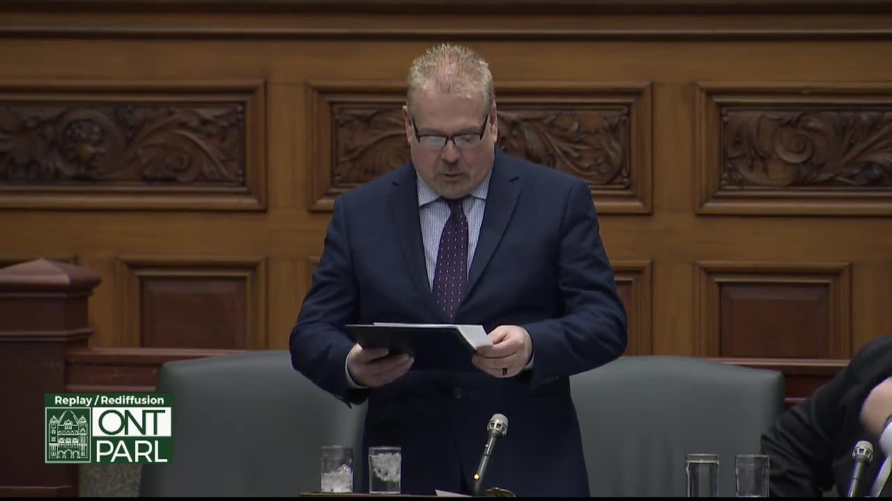 A man in a suit, likely in the Legislative Assembly of Ontario, reads from a document held in a black folder. He's standing at a podium, with a microphone in front of him.
A man in a suit, likely in the Legislative Assembly of Ontario, reads from a document held in a black folder. He's standing at a podium, with a microphone in front of him.