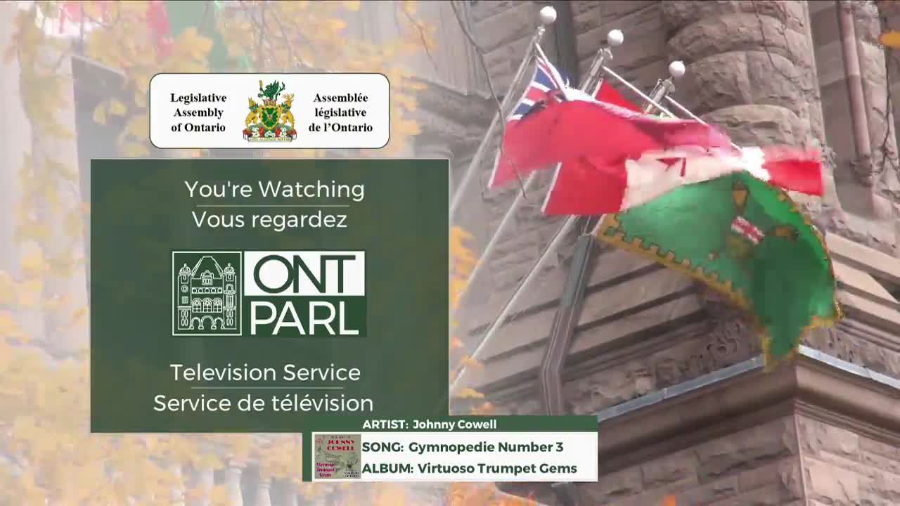 The Ontario flag and the Canadian flag snap in the wind against the stone facade of the Legislative Assembly. A green overlay displays "ONT PARL Television Service" and credits a song.