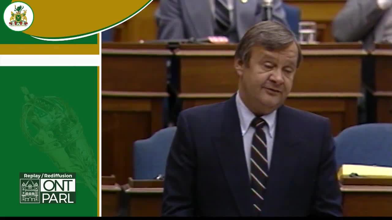 A man in a dark suit and striped tie speaks from a wooden podium. The Legislative Assembly of Ontario's crest appears in the upper left corner.