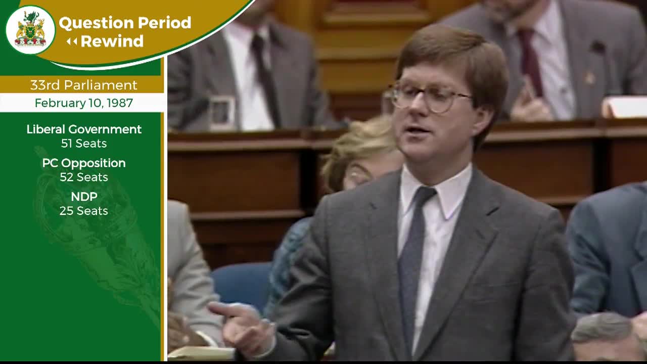 A man in a suit and tie speaks, gesturing with his hand. Behind him, other figures sit in tiered seating within the Legislative Assembly of Ontario.