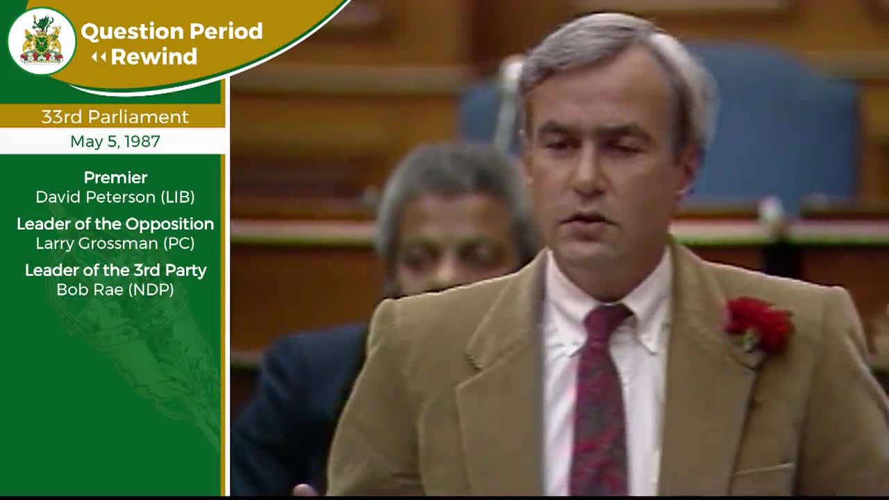 The man in the tan jacket leans forward, his gaze fixed on something just out of frame. Behind him, another man with grey hair watches intently.