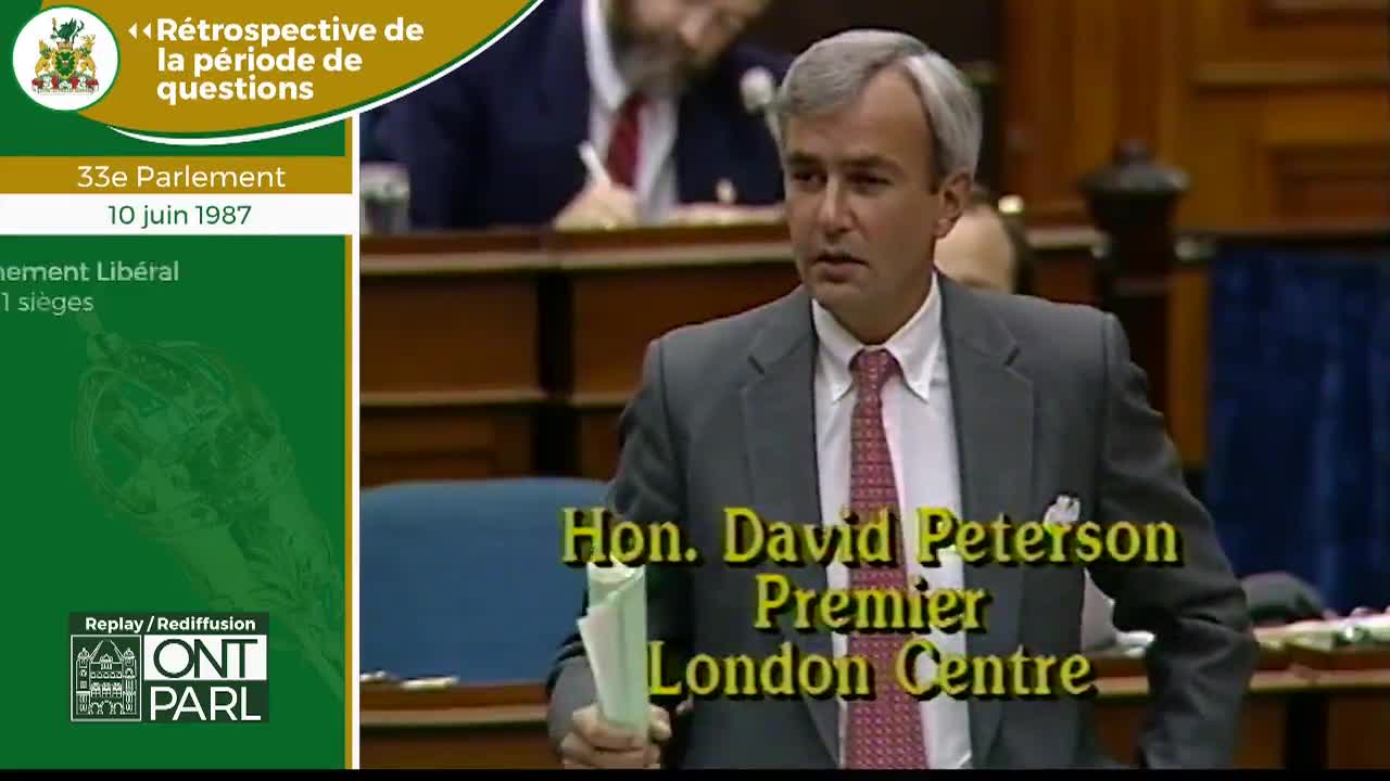The Premier of Ontario, David Peterson, stands in the Legislative Assembly, holding a few papers. He looks towards someone off-camera, his expression attentive.