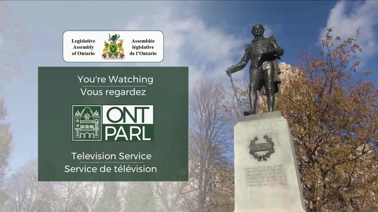A bronze statue of a man in historical dress stands on a stone pedestal. Behind him, bare branches of trees reach towards a bright blue sky.