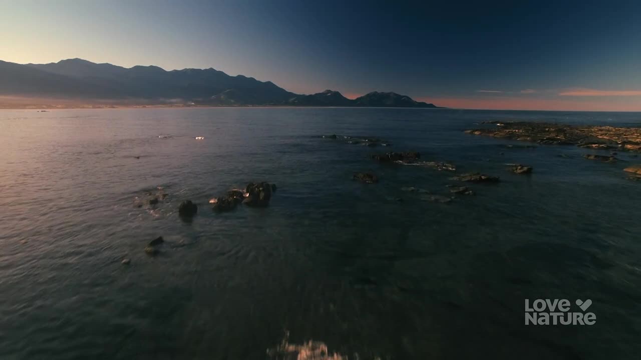 The ocean stretches out towards a distant mountain range, the water's surface reflecting the fading light. Dark rocks break the surface of the water, creating a natural barrier.
The ocean stretches out towards a distant mountain range, the water's surface reflecting the fading light. Dark rocks break the surface of the water, creating a natural barrier.