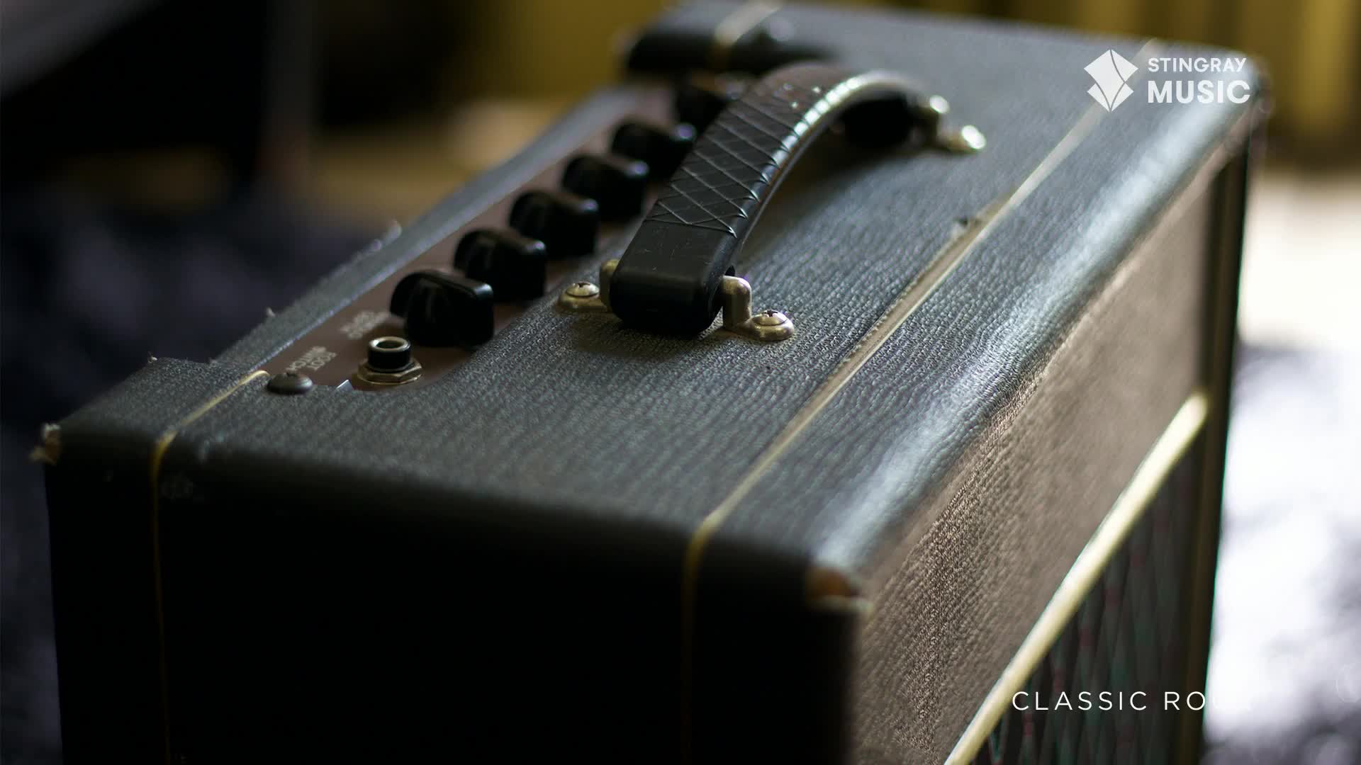 The black guitar amplifier sits quietly, its knobs and handle in sharp focus. A Stingray Music logo hints at the classic rock tunes about to fill the room.
