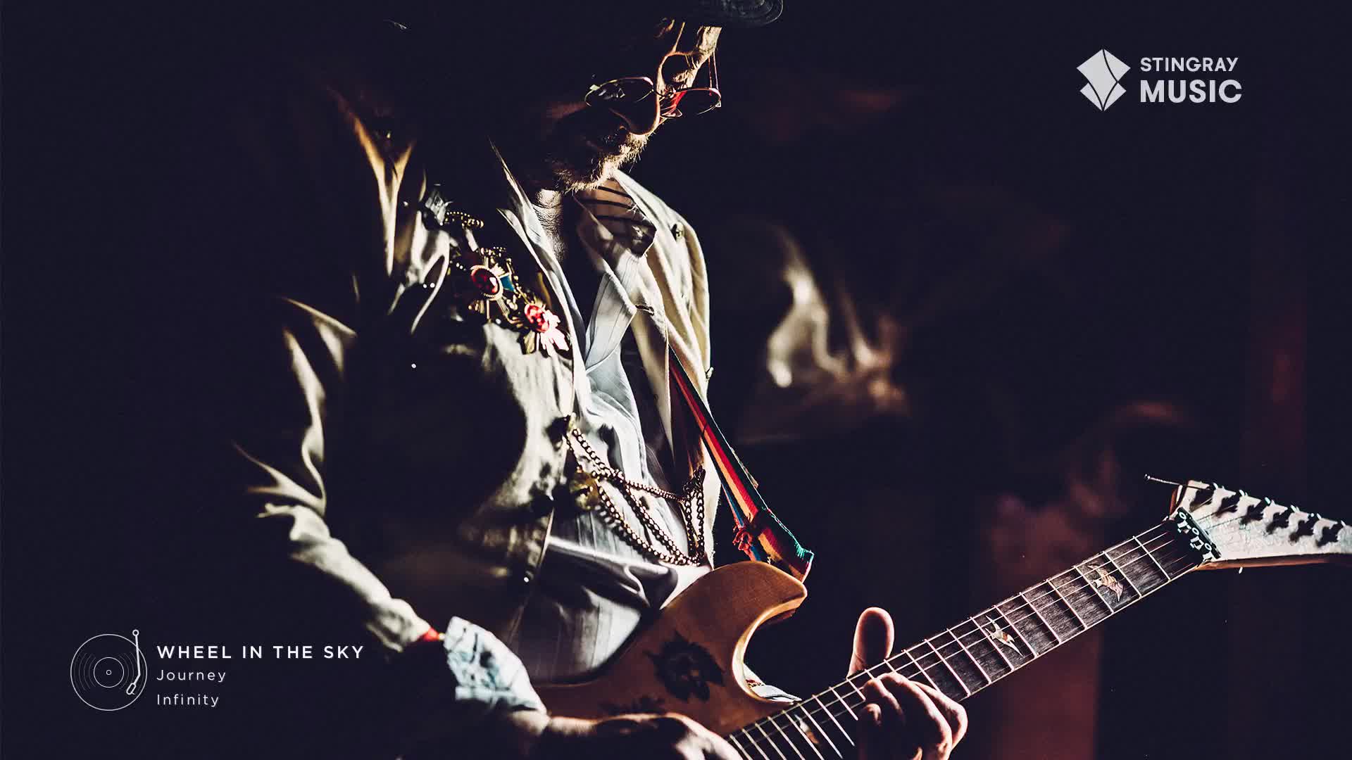 A musician, bathed in stage light, strums a decorated guitar, his fingers dancing across the fretboard. The Stingray Classic Rock logo sits in the corner, and the song "Wheel in the Sky" by Journey fills the air.
