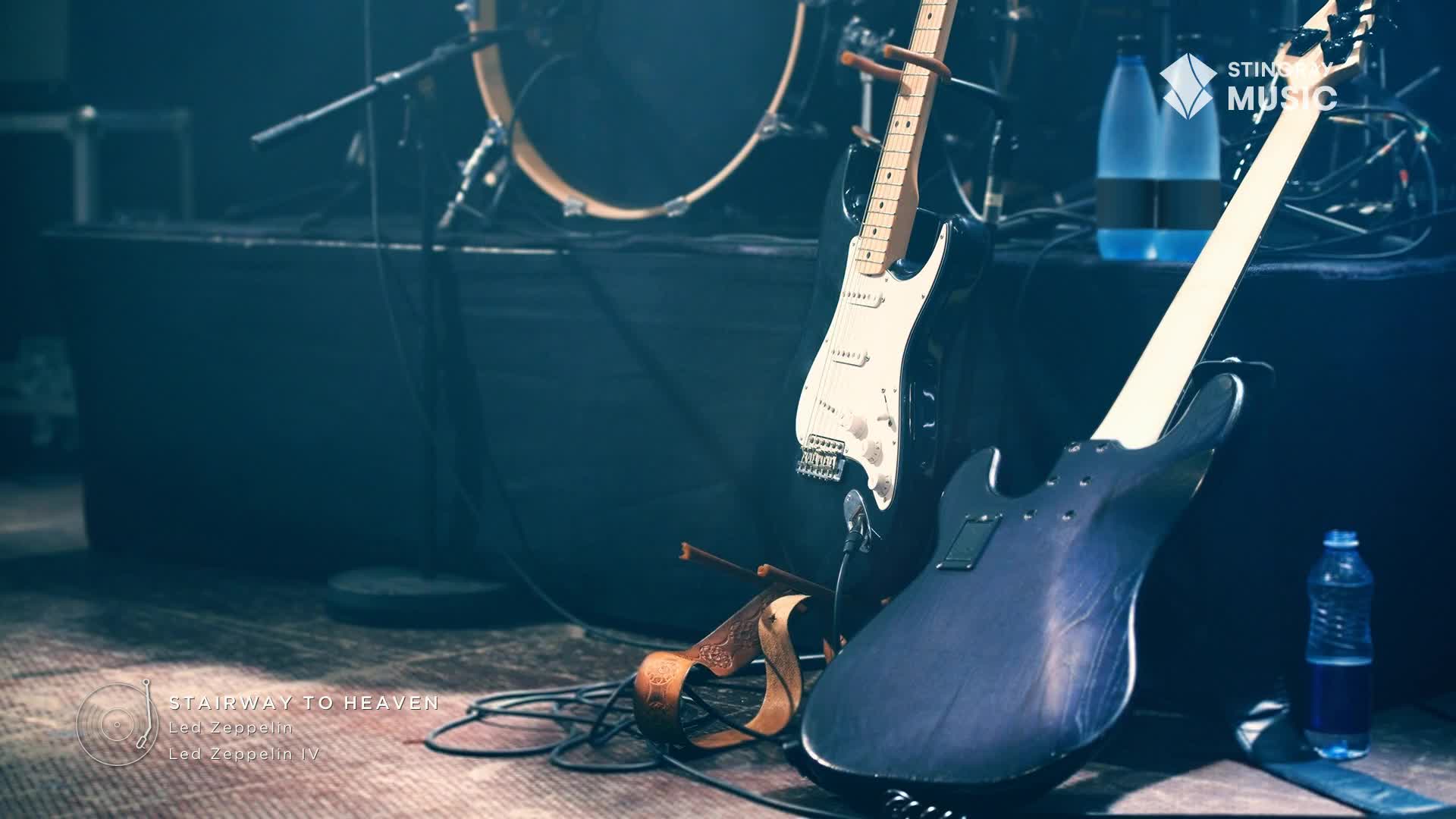 Two guitars lean against the stage, waiting for the Stingray Classic Rock show to start. A drum kit sits in the background, and a water bottle is on the floor, ready for the musicians.
