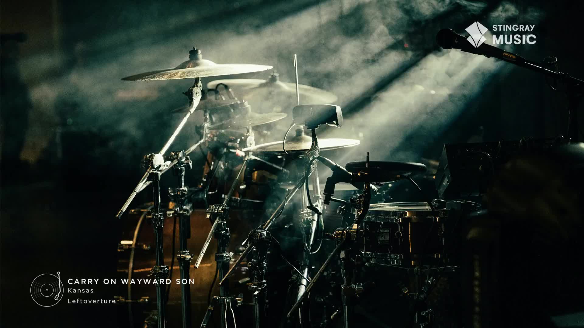 The drum kit is center stage, bathed in light and smoke, ready for a performance on Stingray Classic Rock. The cymbals gleam as the drummer prepares to launch into "Carry on Wayward Son" by Kansas.
