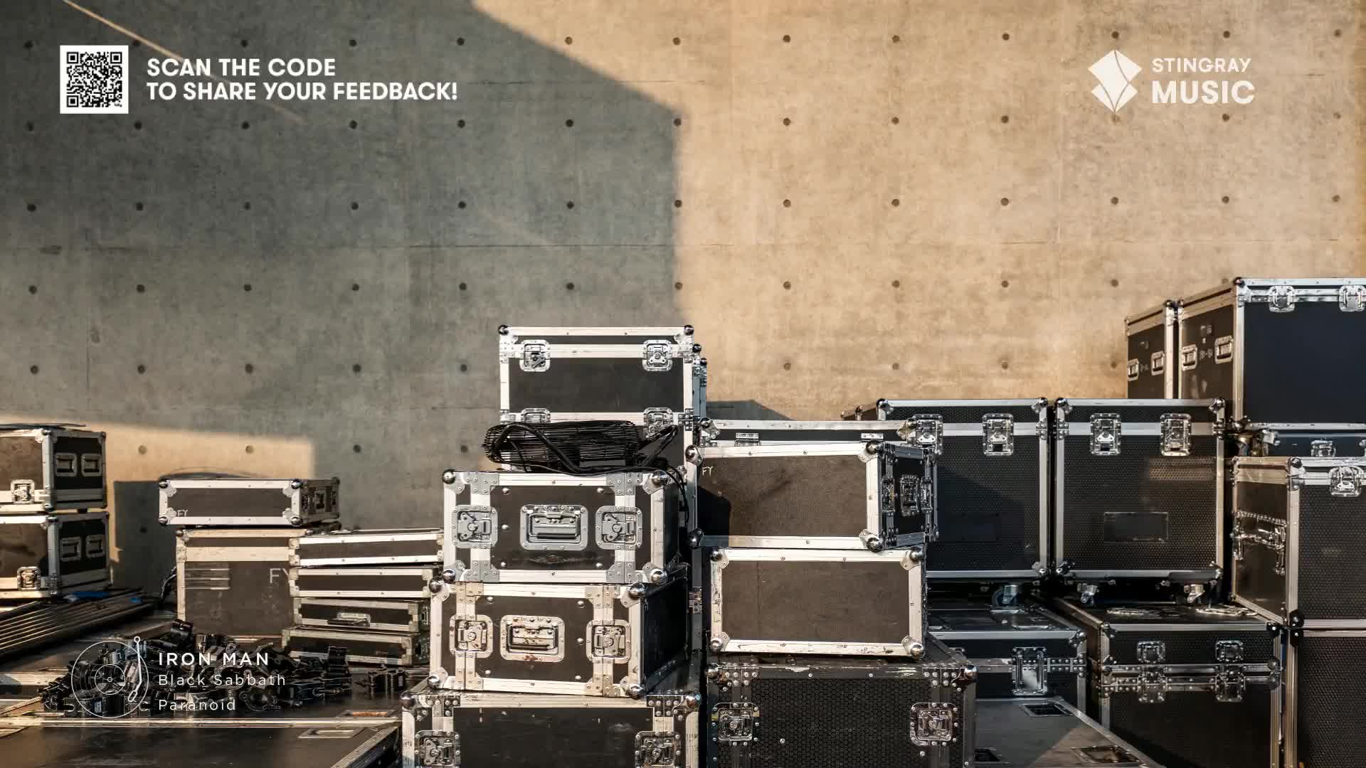 A stack of road cases, ready for the next Stingray Classic Rock show in Canada, sits against a concrete wall. The shadow of the stage equipment falls across the boxes, and the song "Iron Man" by Black Sabbath is playing.
