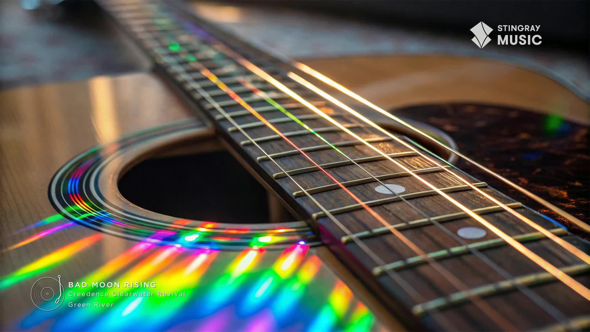 Acoustic guitar strings gleam, reflecting a rainbow of colors across the soundhole. The Stingray Music logo sits in the corner, while a classic rock song by Creedence Clearwater Revival is about to start.
