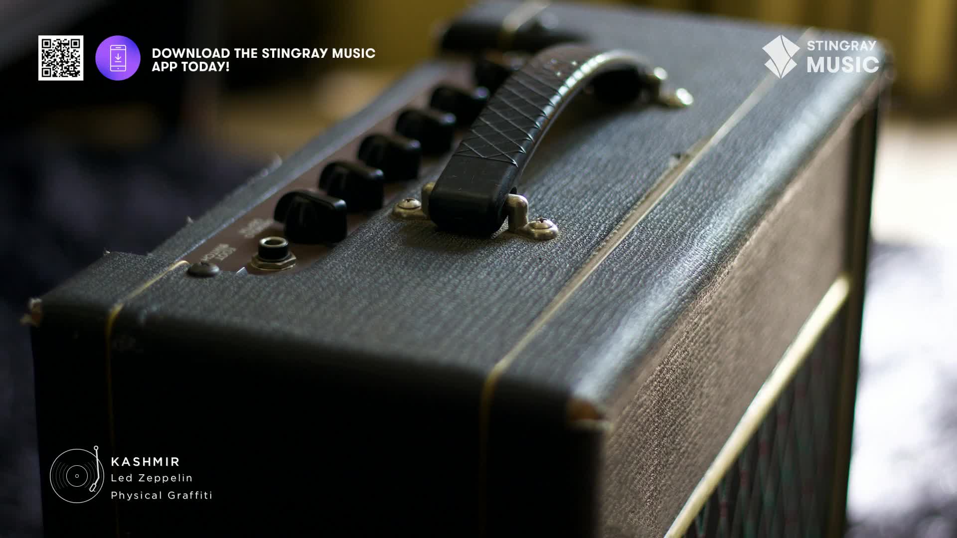 The worn black leather of a guitar amplifier sits in the foreground, its knobs and handle clearly visible. The Stingray Music logo and a QR code for the app are in the top corner, while the song "Kashmir" by Led Zeppelin is listed below.
The worn black leather of a guitar amplifier sits in the foreground, its knobs and handle clearly visible. The Stingray Music logo and a QR code for the app are in the top corner, while the song "Kashmir" by Led Zeppelin is listed below.