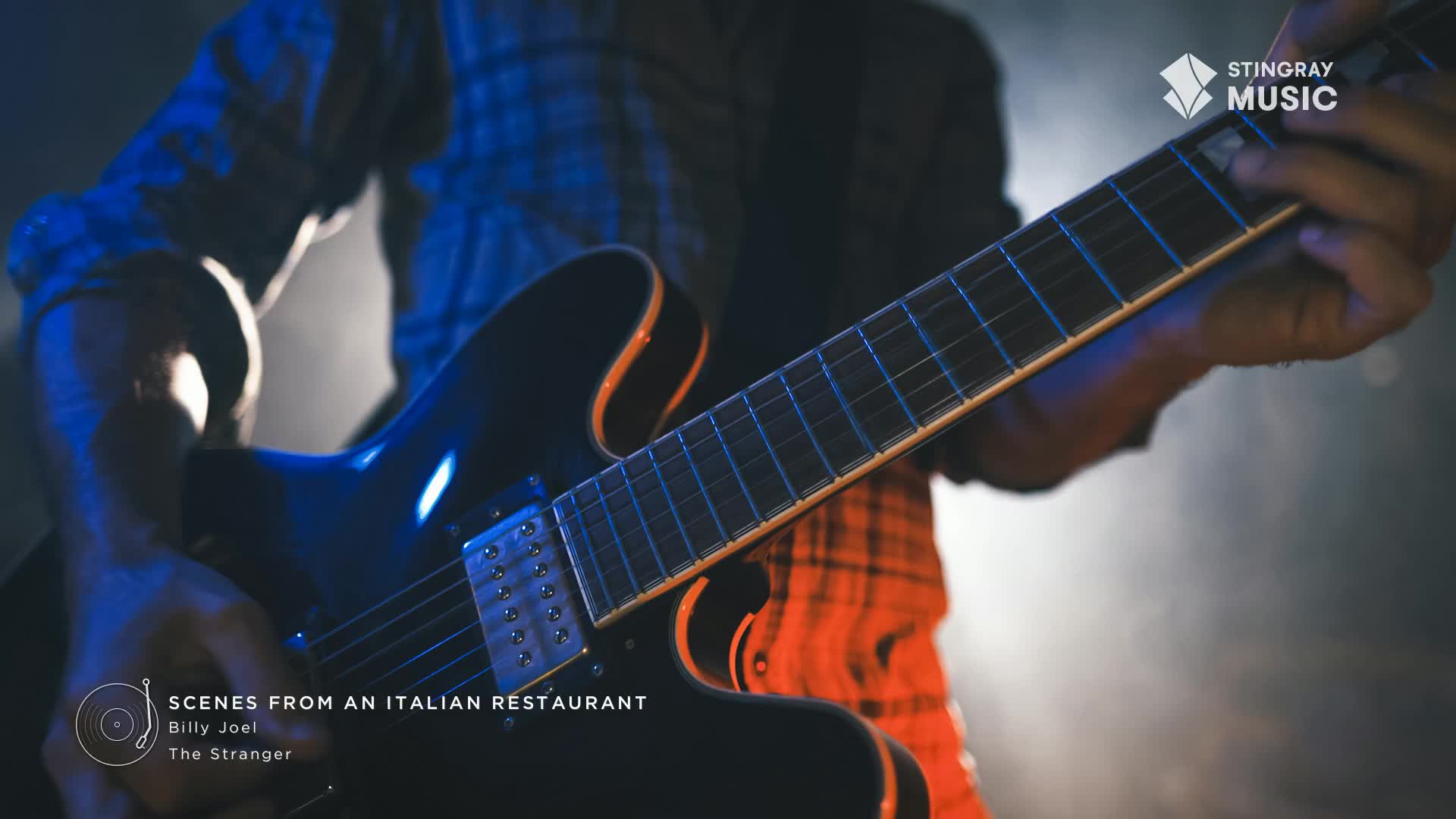A guitarist's hands move across the fretboard of a black electric guitar, bathed in the warm glow of stage lights. The iconic Stingray Music logo sits in the corner, hinting at a classic rock performance.