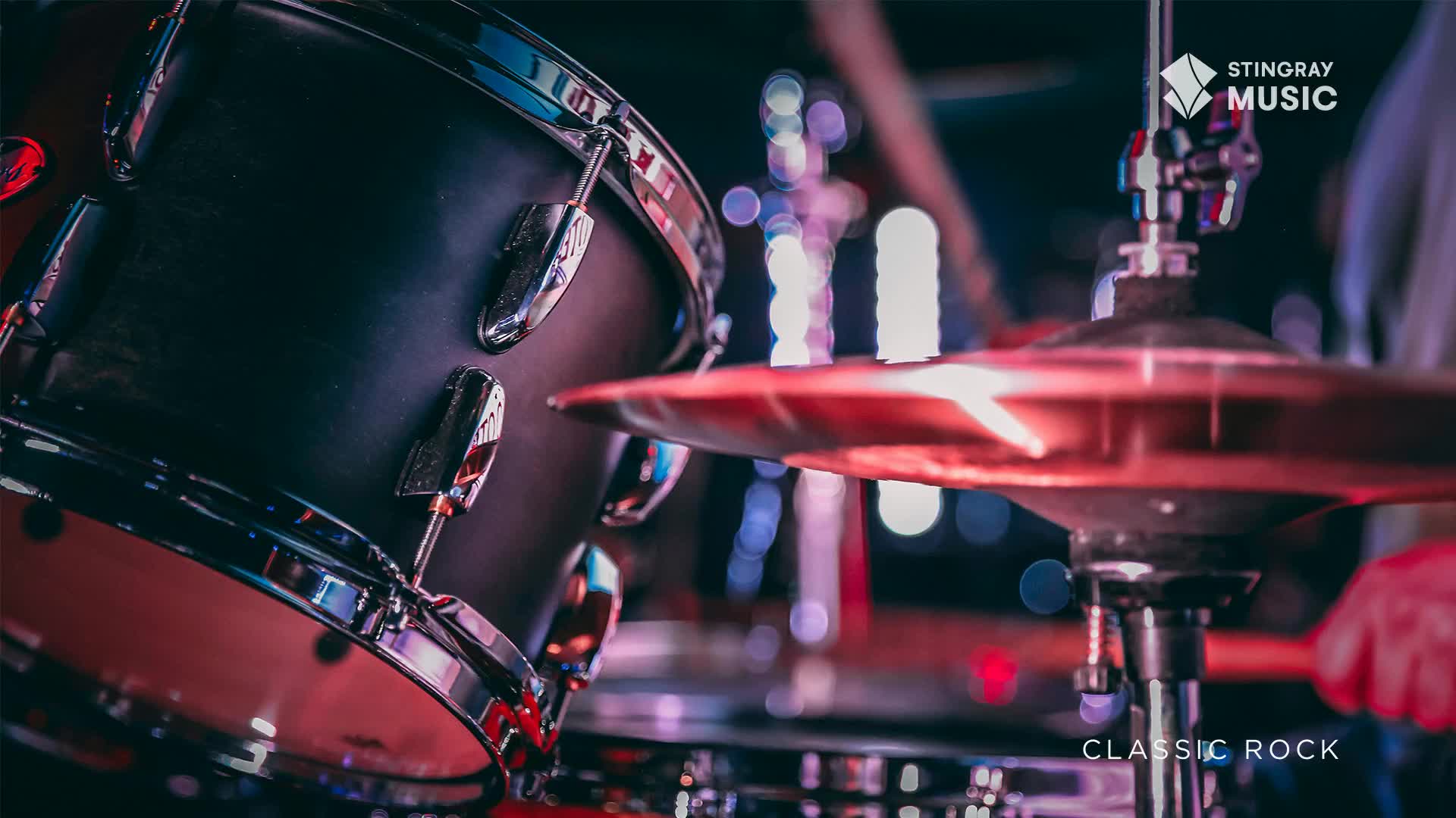 A drumstick is about to strike a cymbal, its red glow reflecting off the metal. The bass drum, dark and imposing, sits ready for the beat.