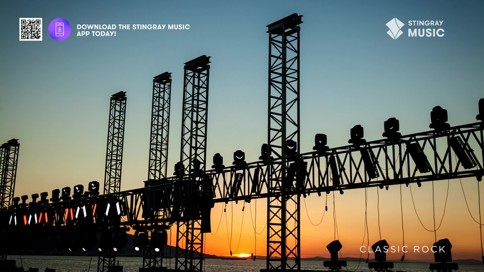 The sun dips below the horizon, casting a warm glow behind a row of towering stage lights. Cables hang from the metal truss, ready for the Stingray Classic Rock concert.