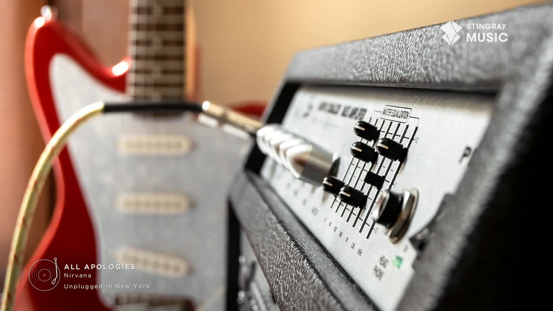 A red electric guitar is plugged into a black amplifier. The amp's knobs are set for a Stingray Classic Rock sound.