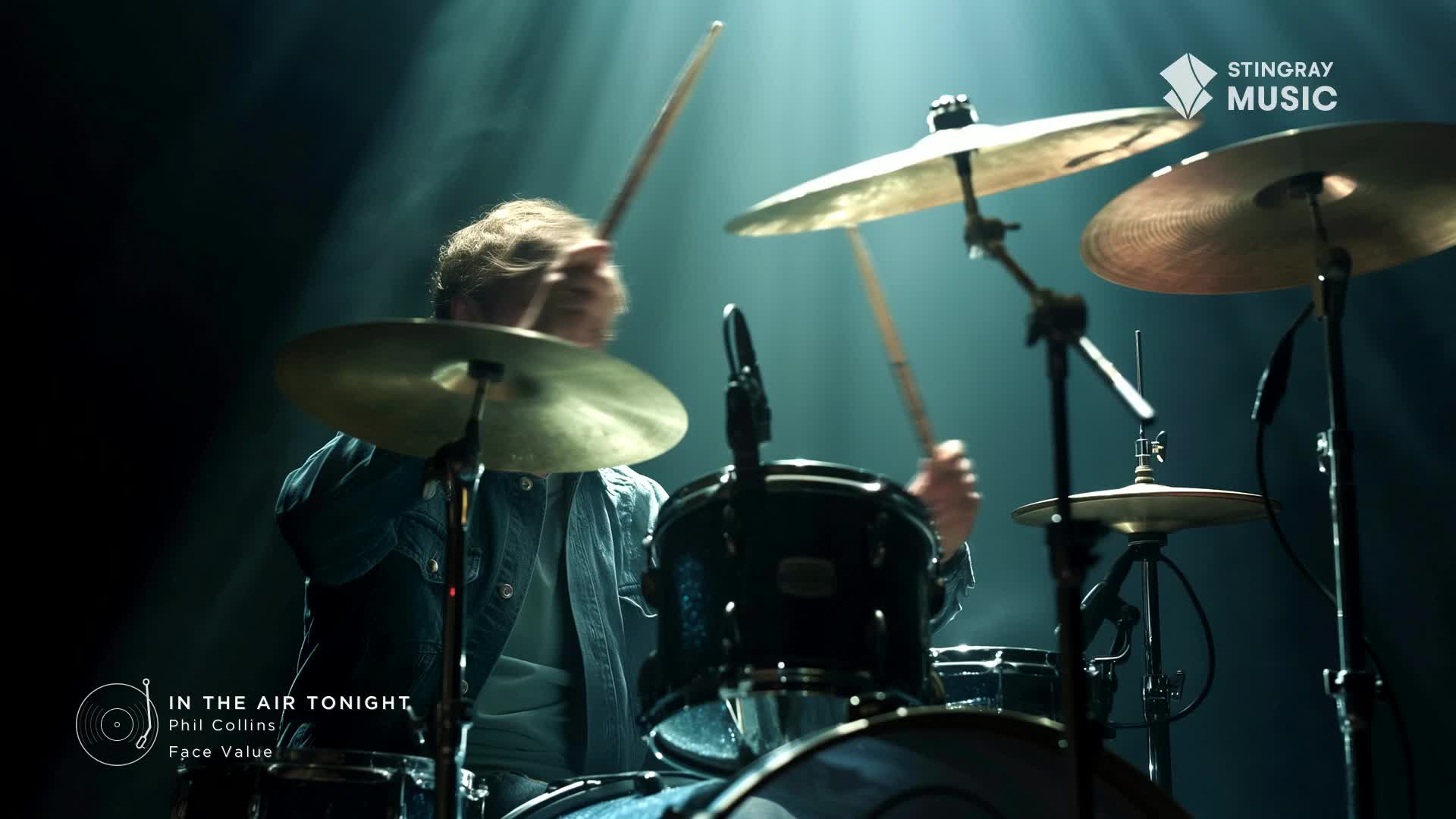 Drumsticks fly as the beat for "In the Air Tonight" pounds out. The musician's denim jacket is a blur against the stage lights.