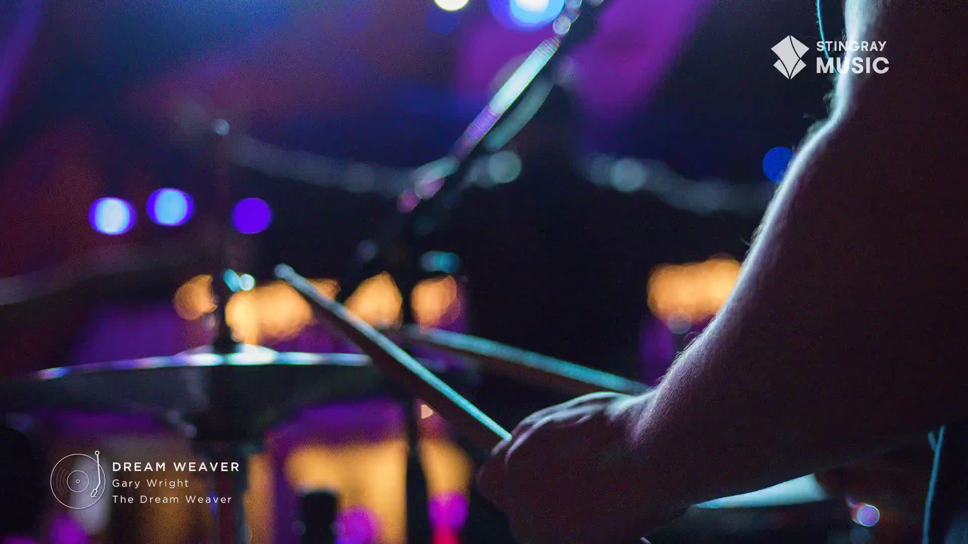 Drumsticks are poised over a cymbal, ready to strike. The stage lights cast a purple and blue glow on the scene, hinting at a classic rock performance in Canada.