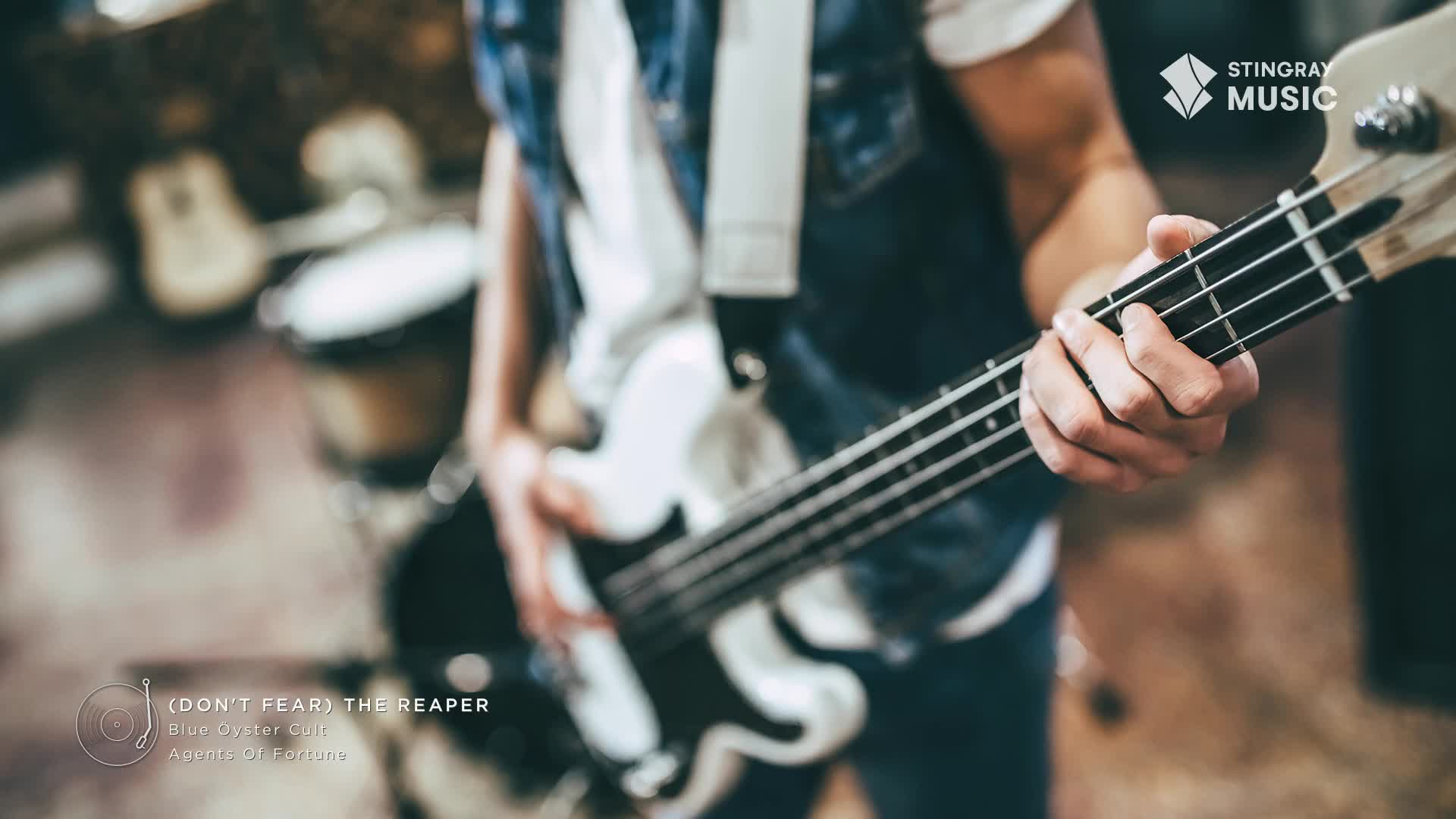 Fingers dance across the fretboard of a white bass guitar, the sound of Blue Öyster Cult's "(Don't Fear) The Reaper" filling the air. A drummer is visible in the background, ready to lay down the beat.