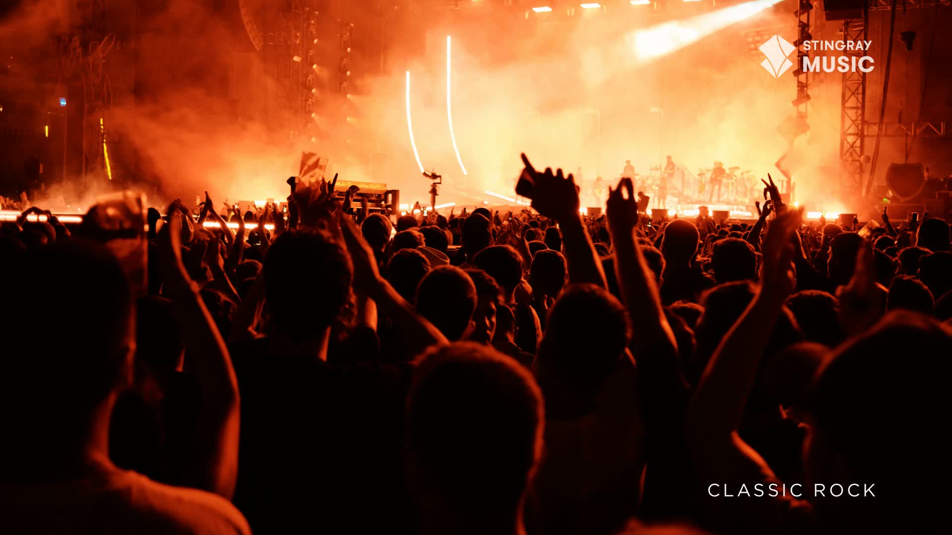 The stage lights blaze orange as a band plays for a massive crowd in Canada.  Hands are raised in the air, silhouetted against the intense glow of the classic rock concert.
