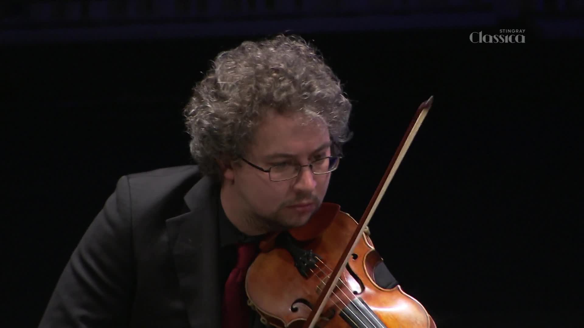 The violinist's bow glides across the strings, drawing out a rich, warm tone.  His intense gaze is fixed on the instrument, as the music fills the space, broadcast by Stingray Classica from Canada.
