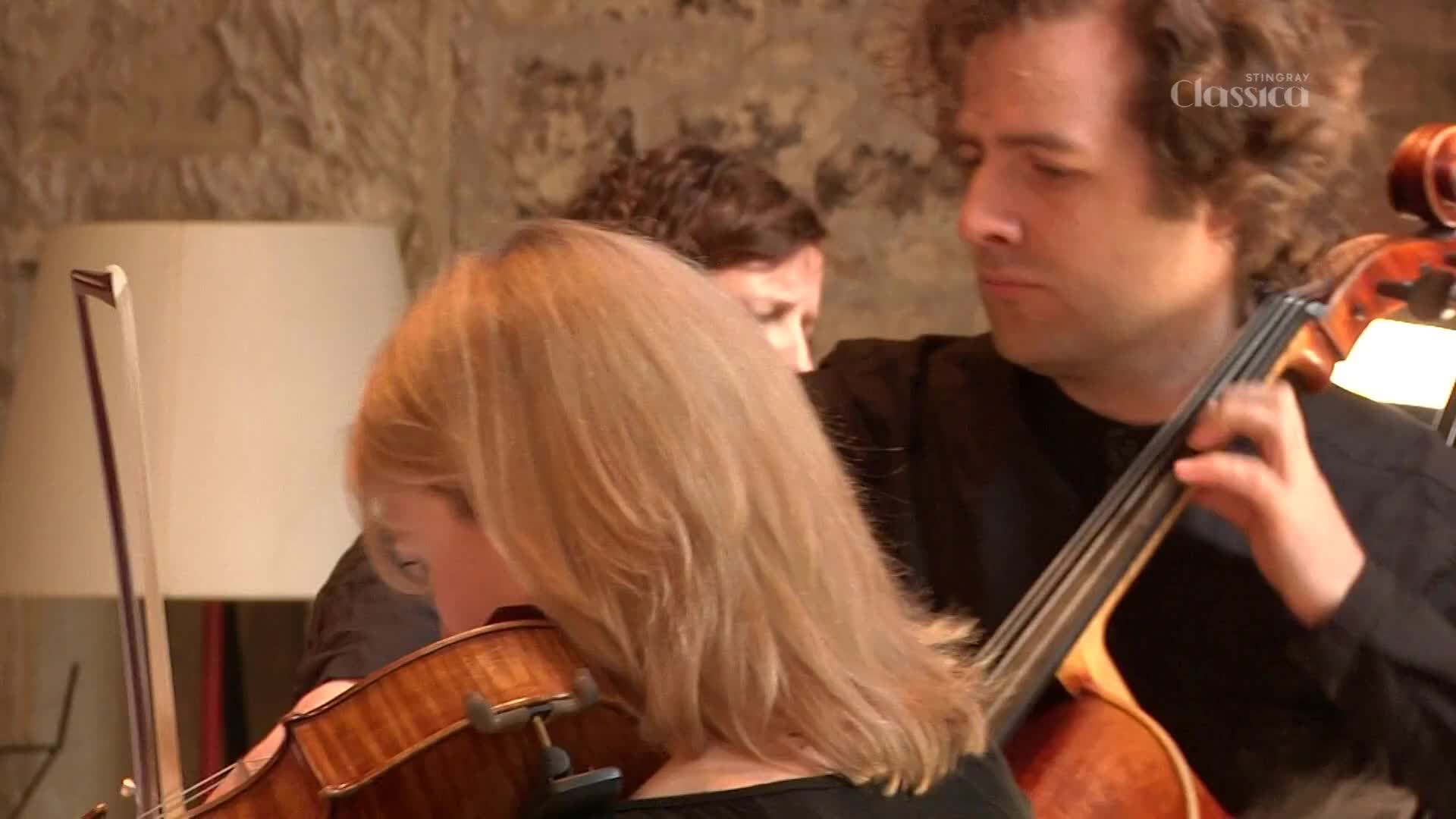 The violinist's bow glides across the strings, while the cellist's fingers dance on the fretboard.  They're focused, playing together, likely for a Stingray Classica broadcast.
