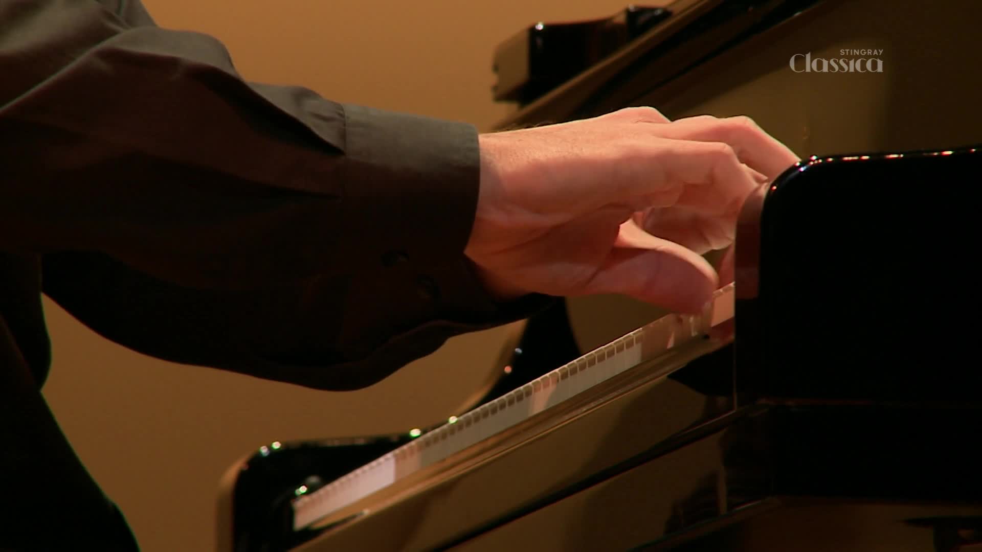 A hand, dressed in a dark sleeve, moves across the piano keys, pressing down with precision. The Stingray Classica logo is visible in the corner, suggesting a broadcast from Canada.
