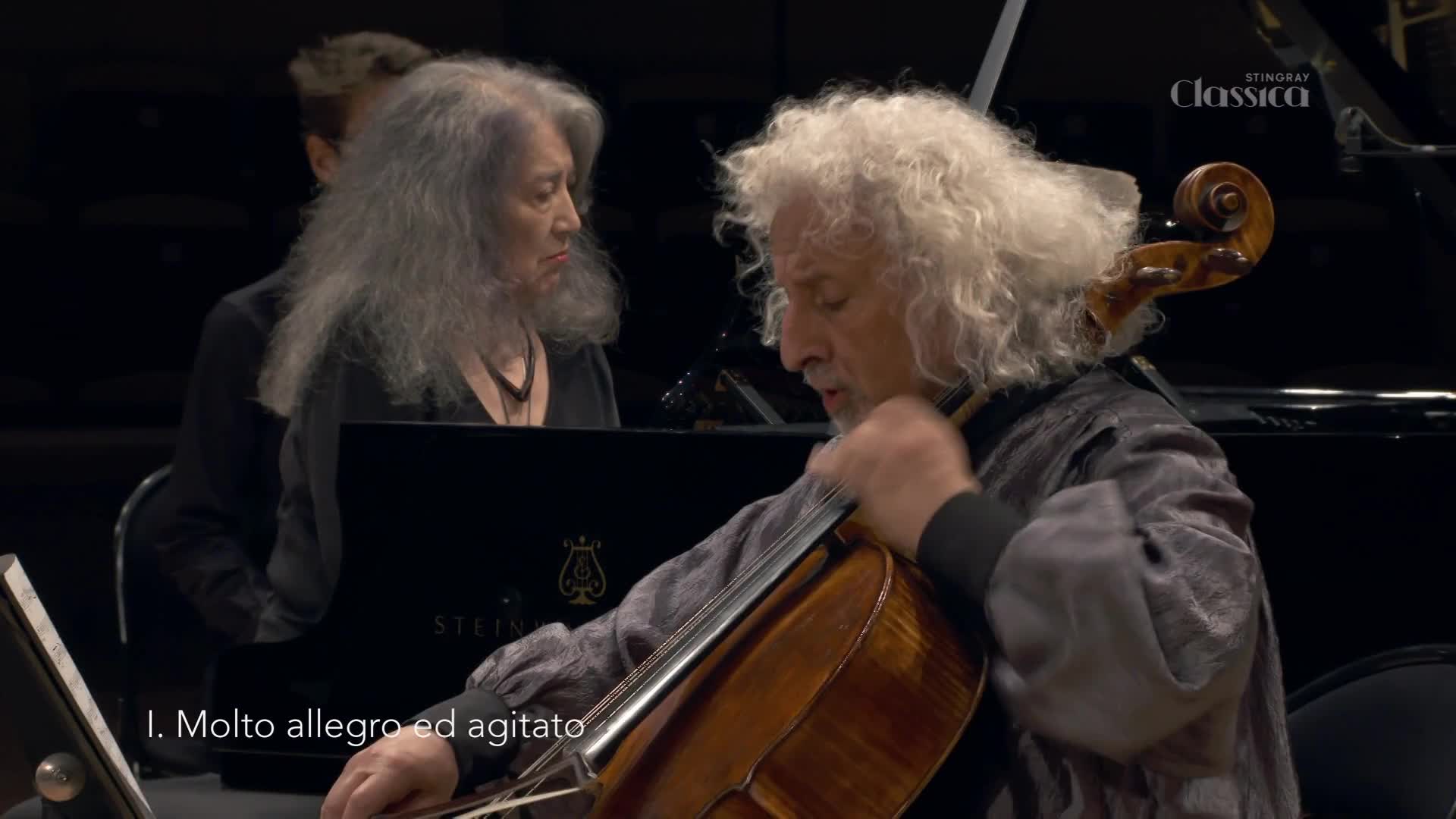 The cellist, with his wild white hair, leans into his instrument, the bow moving across the strings. Beside him, the pianist watches intently, her gaze fixed on the music.
