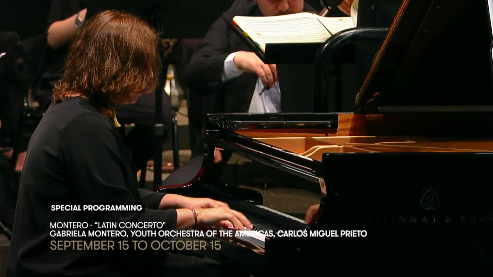 A pianist's hands dance across the keys of a grand piano, while an orchestra member in the background adjusts his sheet music. The screen shows a special program on Stingray Classica, featuring Gabriela Montero performing a "Latin Concerto."

