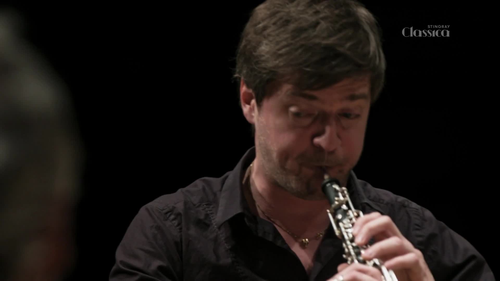 The oboe player's cheeks puff out as he blows, fingers dancing over the keys. A Stingray Classica logo floats in the corner, a reminder of the performance's origin in Canada.
