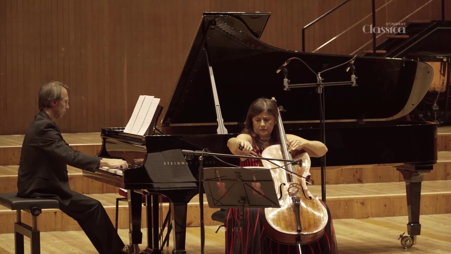 A woman with a cello is drawing the bow across the strings, while a man at the piano accompanies her. The Stingray Classica logo is visible in the upper right corner.
