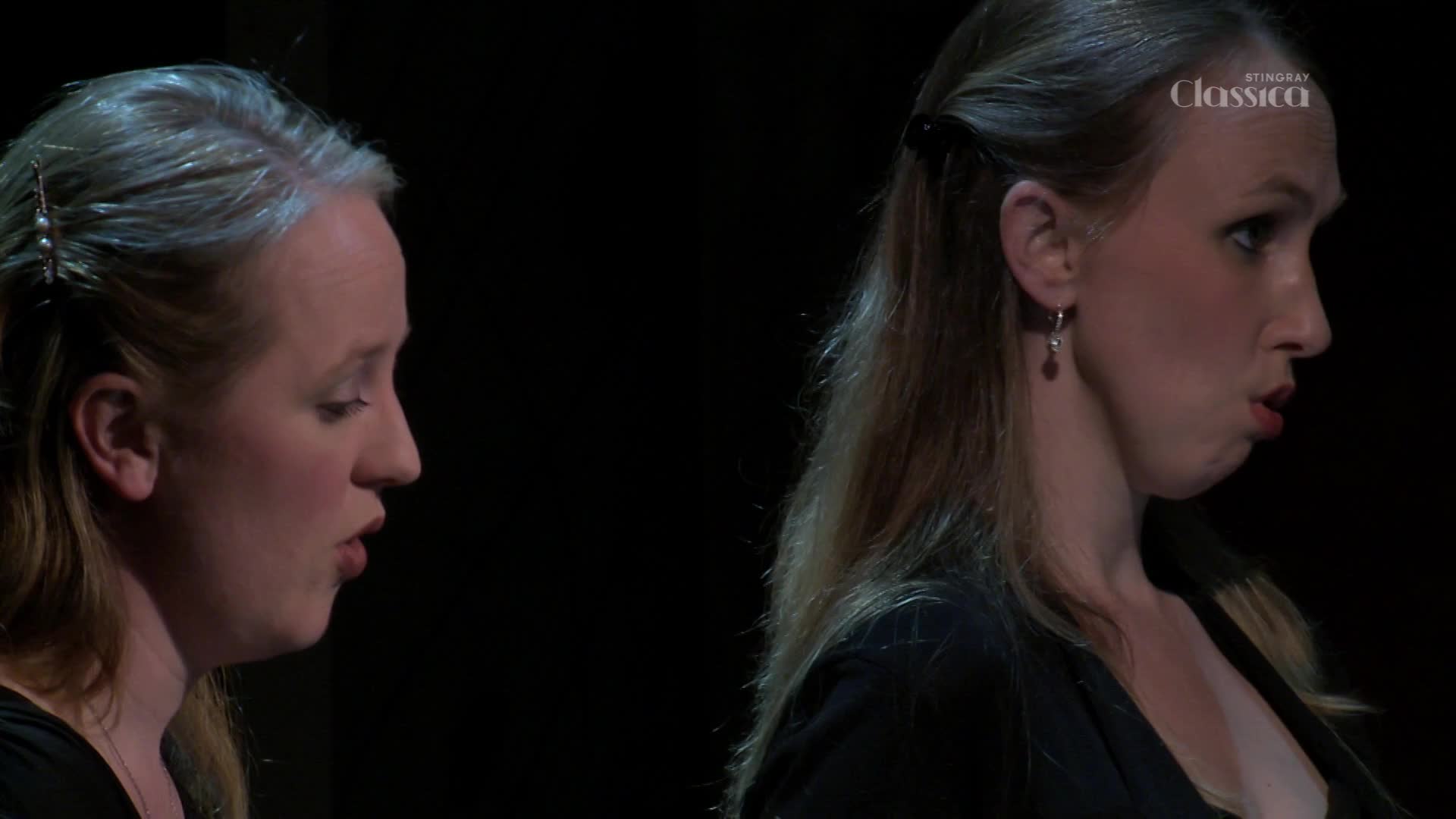 Two women are singing, their faces angled to the side, mouths open. The Stingray Classica logo is visible, suggesting a performance is underway.
