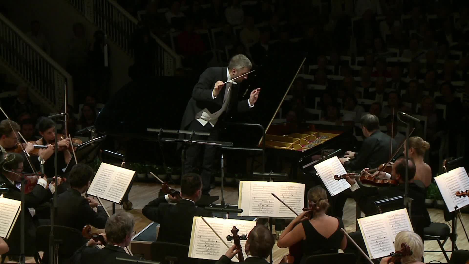 The conductor's baton arcs in the air, guiding the orchestra.  The musicians are focused on their sheet music, their bows moving across the strings.

