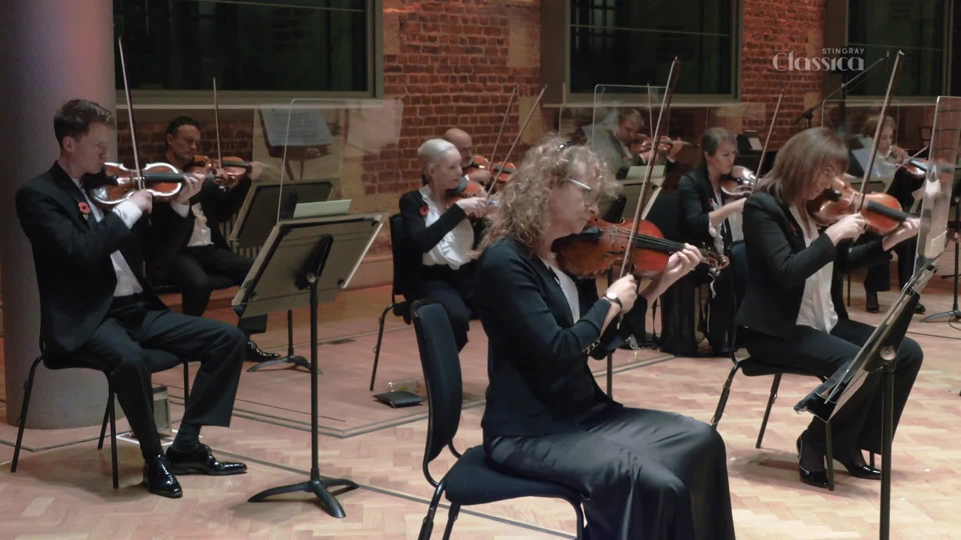 A group of violinists, seated in a brick-walled room, are bowing their instruments in unison. The Stingray Classica logo is visible, suggesting this is a performance being filmed in Canada.
