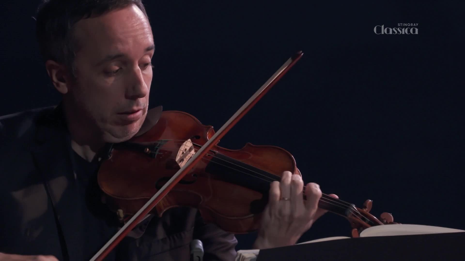 The violinist's bow dances across the strings, making a rich sound.  He's focused on the music, his face illuminated by the glow of the Stingray Classica broadcast from Canada.
