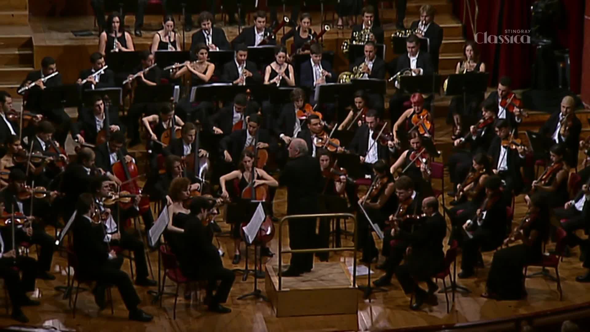 The conductor's arms sweep through the air, directing the musicians. Bows move across strings, and the orchestra is playing on Stingray Classica, from Canada.

