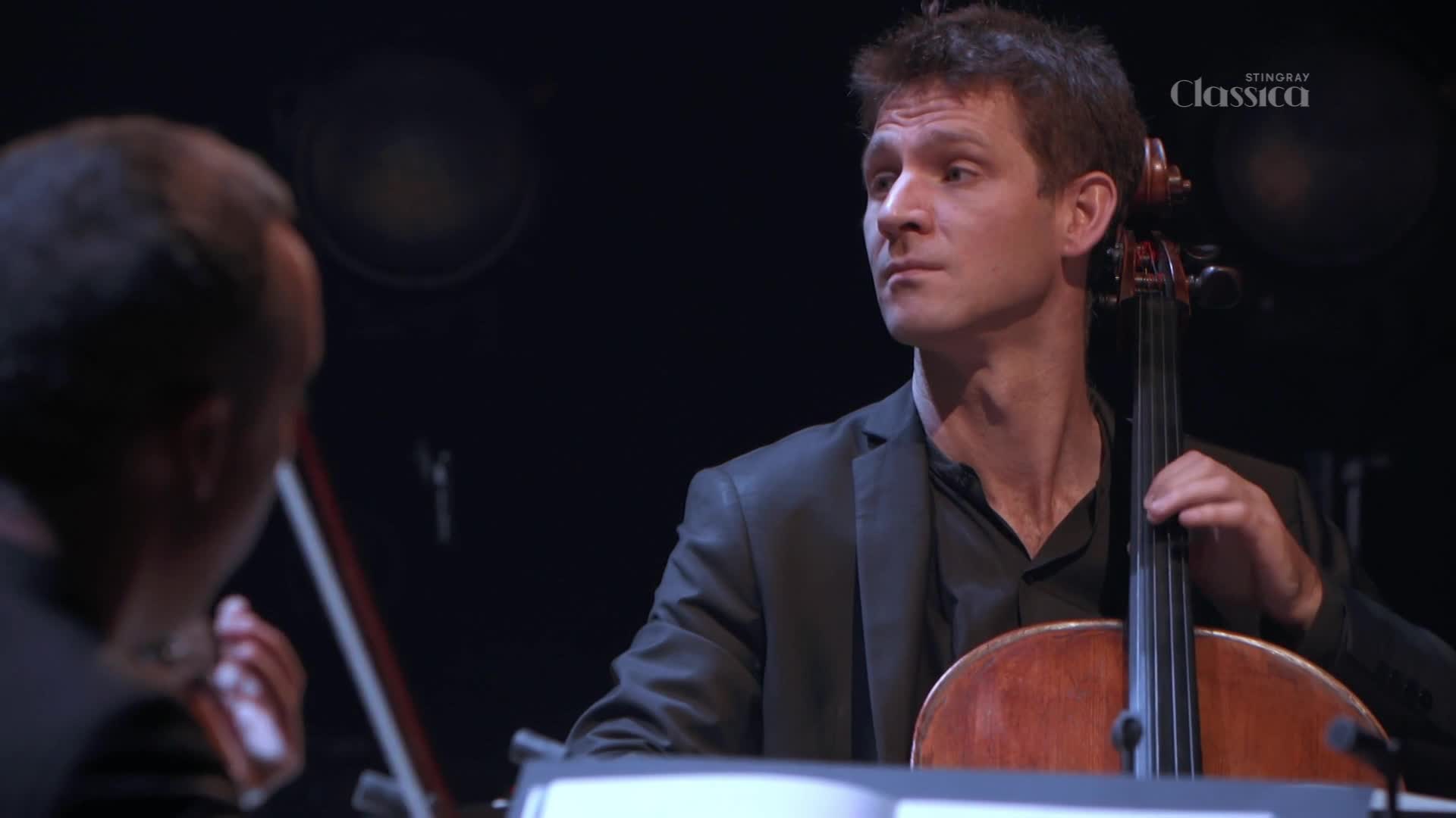 The cellist's bow moves across the strings, drawing out a rich, resonant tone. He's focused, his gaze fixed on the conductor, as the music swells.
