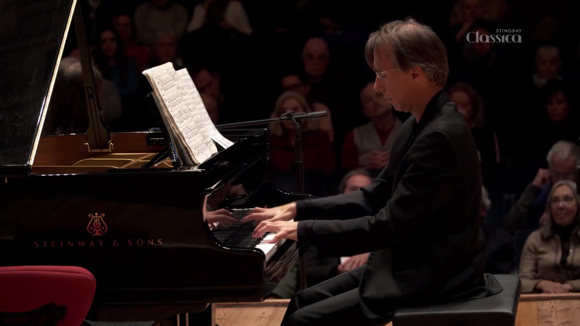 Fingers dance across the keys of a Steinway grand, filling the concert hall with sound. The pianist, focused on the sheet music before him, plays for an attentive audience.