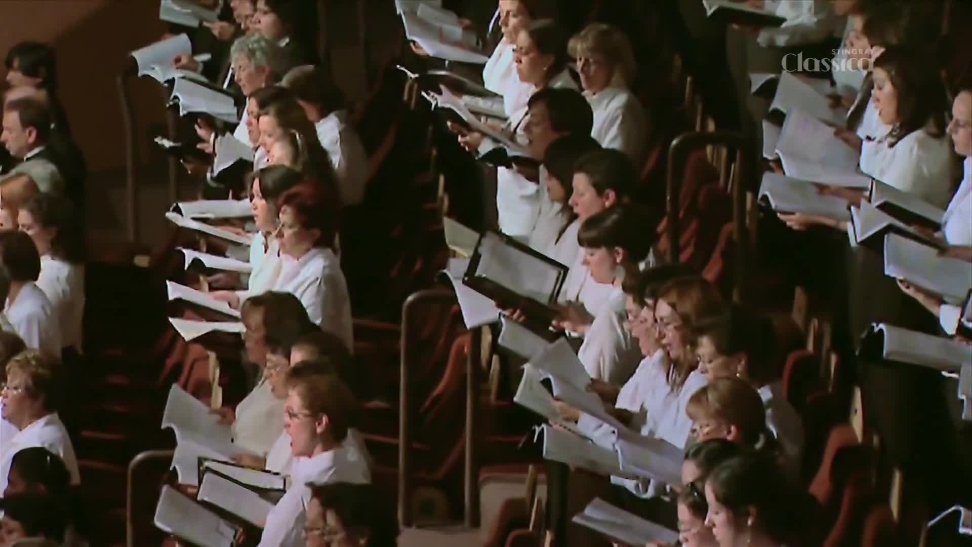 A choir, dressed in white, sings from sheet music. Their voices fill the hall, a rich sound from this Canadian performance.