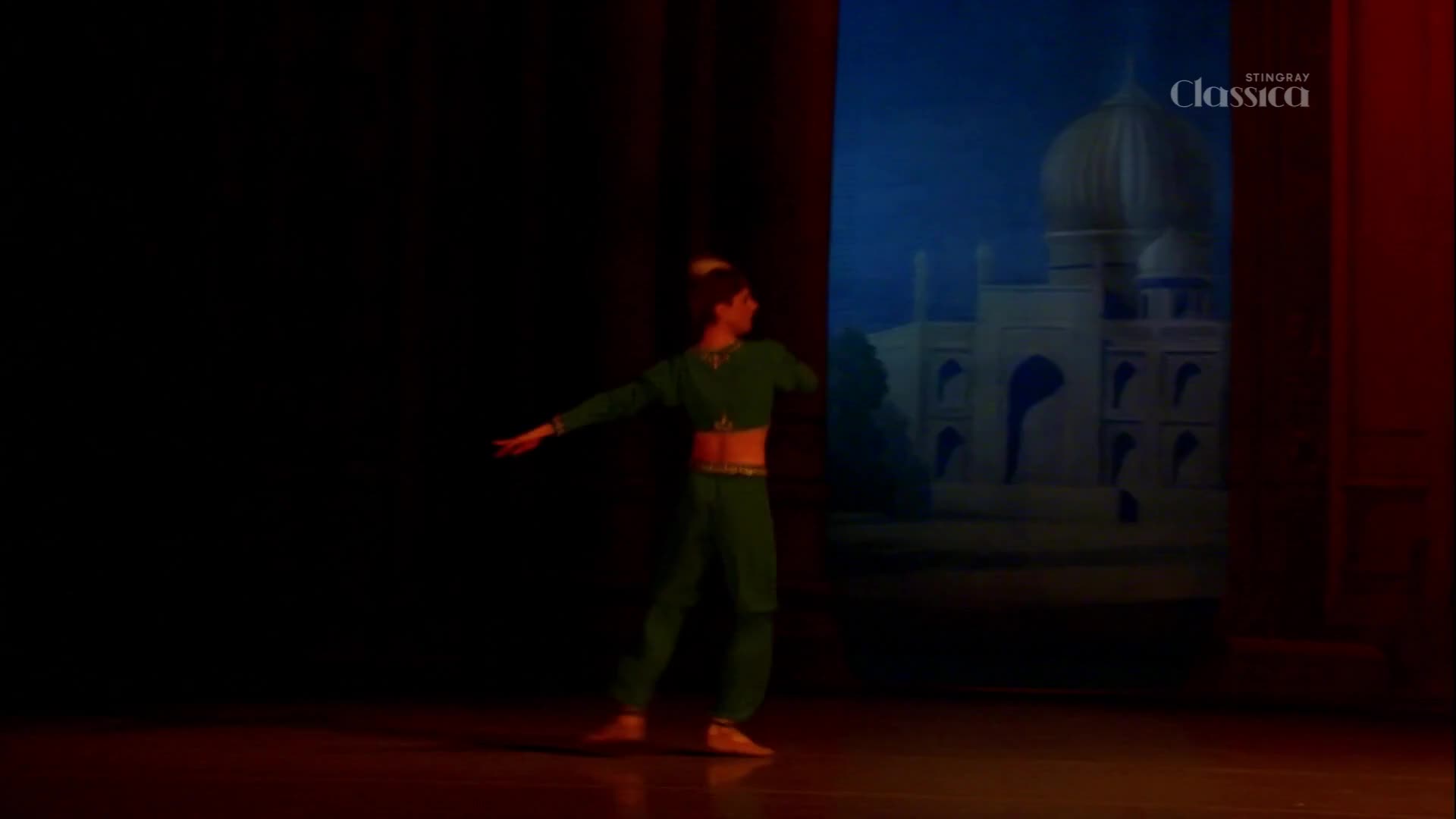 A dancer in green, with a cropped top and flowing pants, extends an arm towards a painted backdrop of a grand Indian palace. The Stingray Classica logo is visible in the upper right corner.