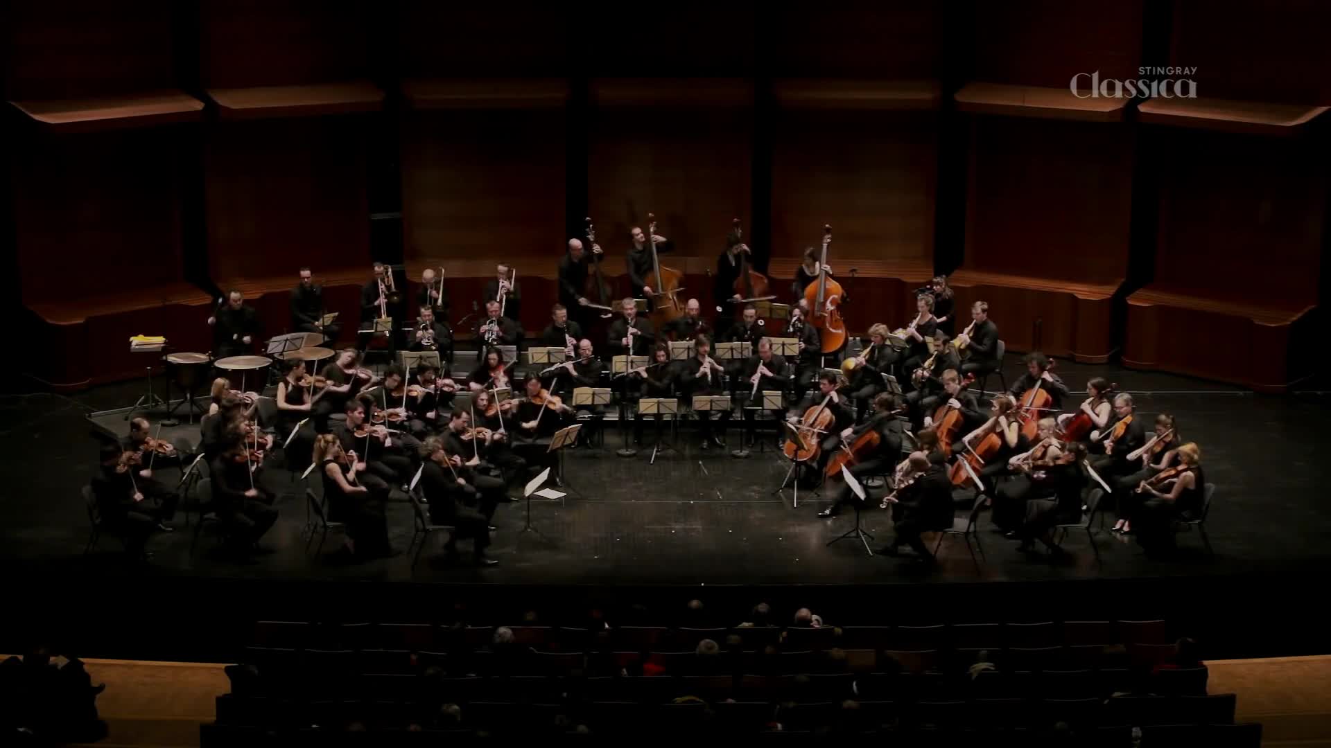 The orchestra is playing on stage, their bows moving in unison across the strings. A Stingray Classica broadcast is being filmed from the balcony.