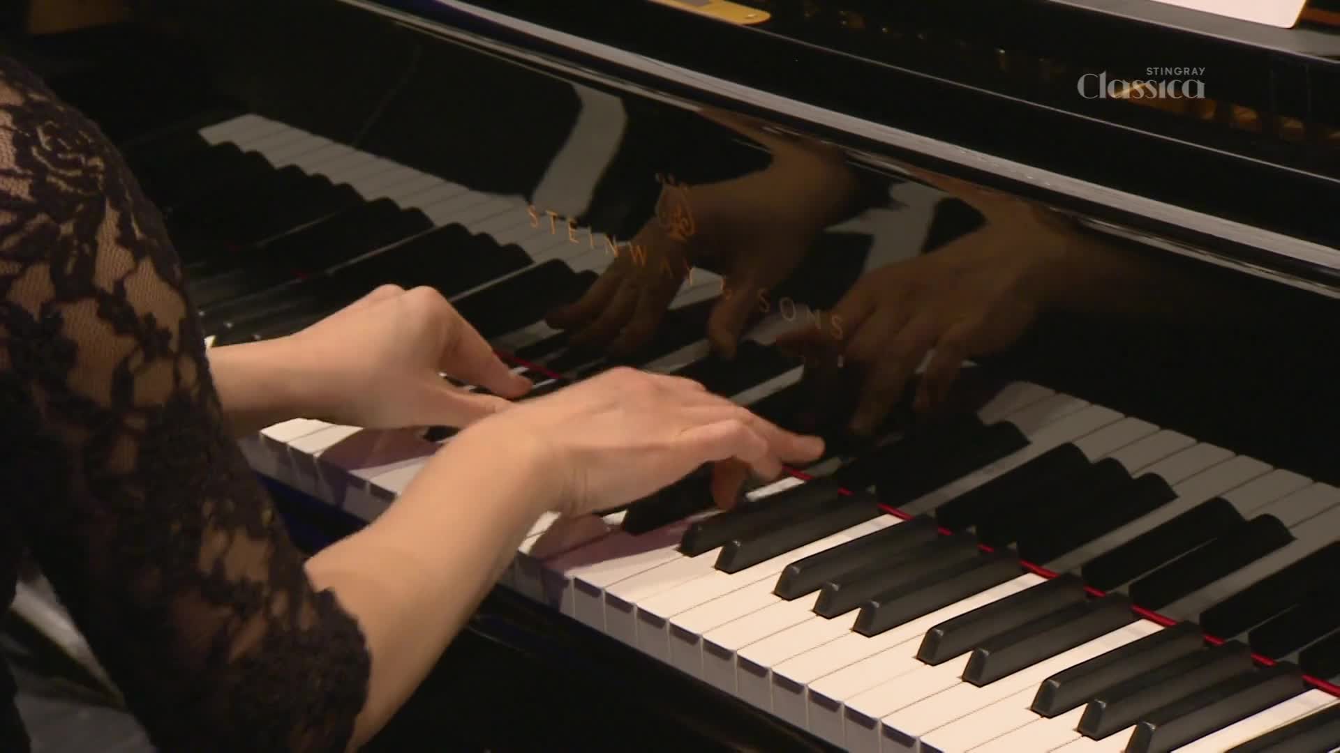 Fingers dance across the black and white keys of a grand piano, their movements reflected in the polished wood. The Stingray Classica logo is subtly visible on the piano's surface.