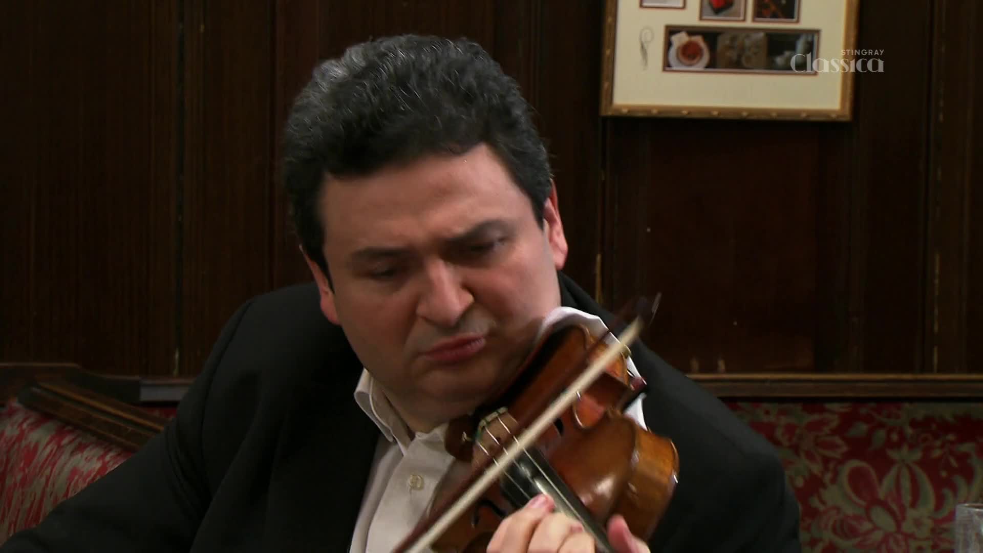 A violinist draws his bow across the strings, his brow furrowed in concentration. The rich wood of his instrument gleams under the lights as he plays.