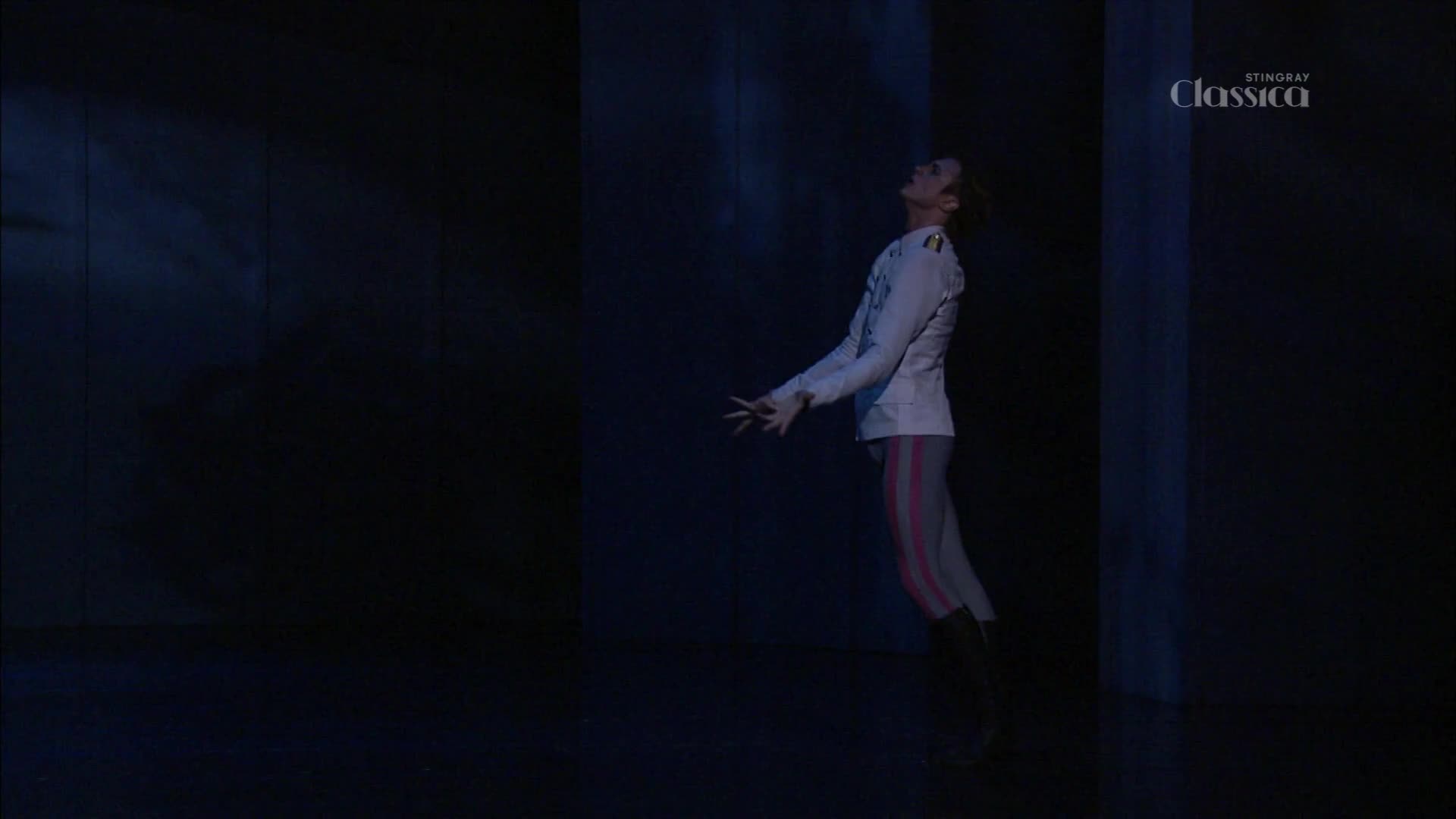 A dancer in a white jacket and striped leggings leans back, arms outstretched. The stage is dark, with a single spotlight illuminating the performer.