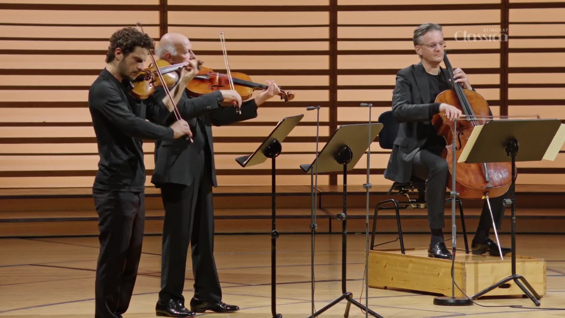 Three musicians are on stage, two playing violins and one a cello. The Stingray Classica logo is visible in the background.