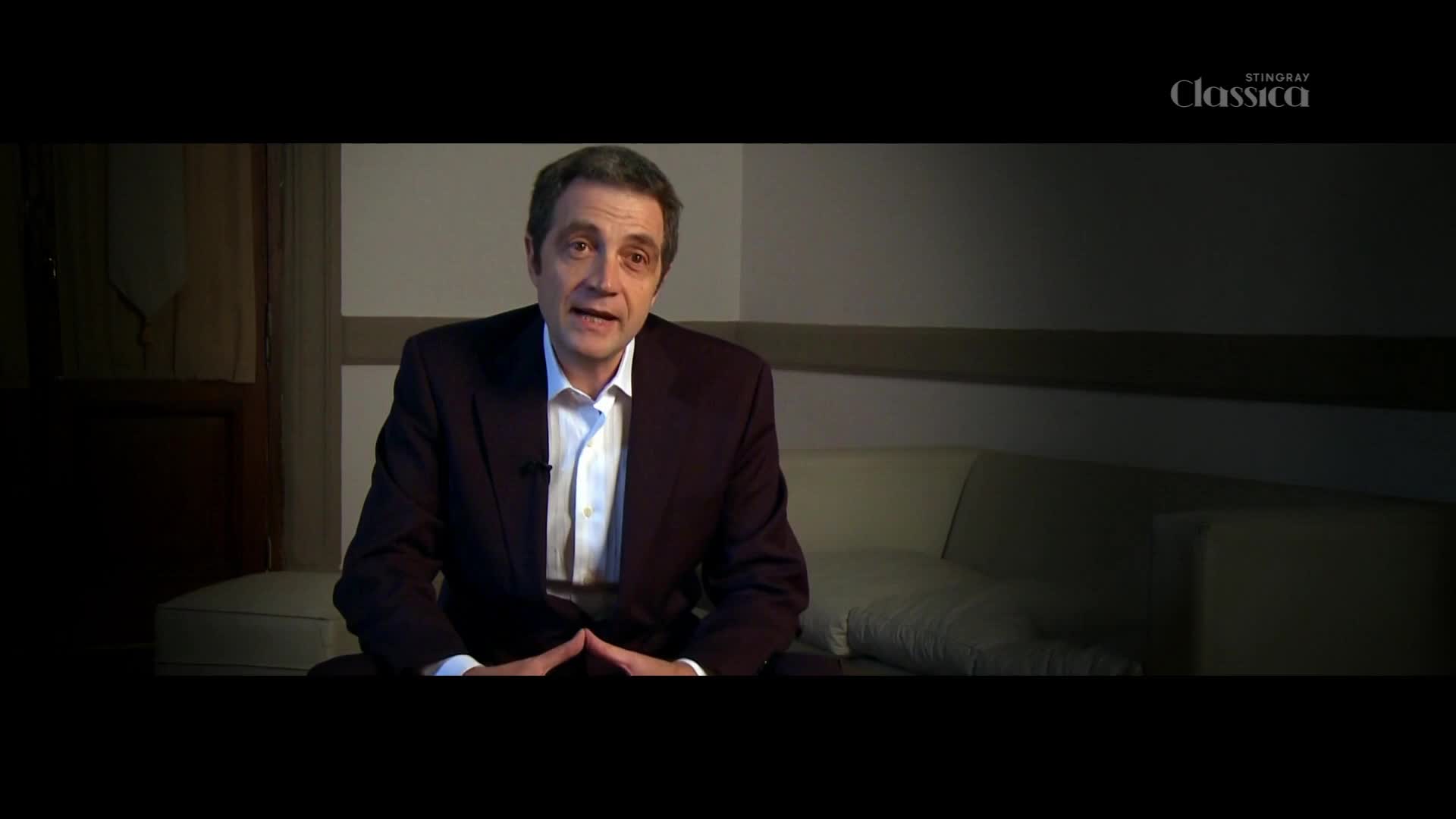 A man in a dark suit and white shirt speaks directly to the camera, his hands clasped in front of him. The Stingray Classica logo appears in the upper right corner.