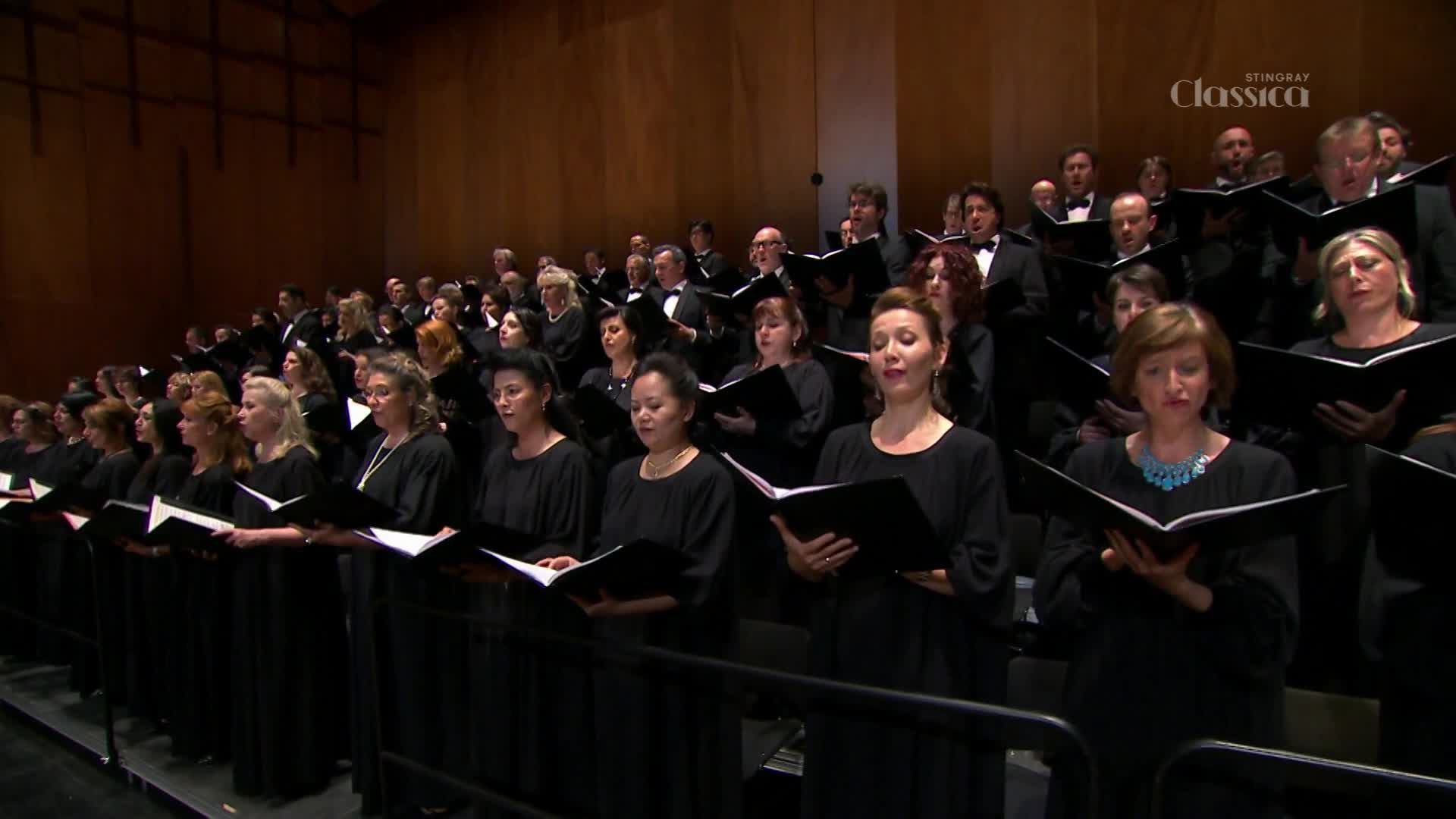 A large choir, dressed in black, stands on risers, their voices filling the concert hall. The Stingray Classica logo is visible in the upper right corner, indicating a broadcast from Canada.