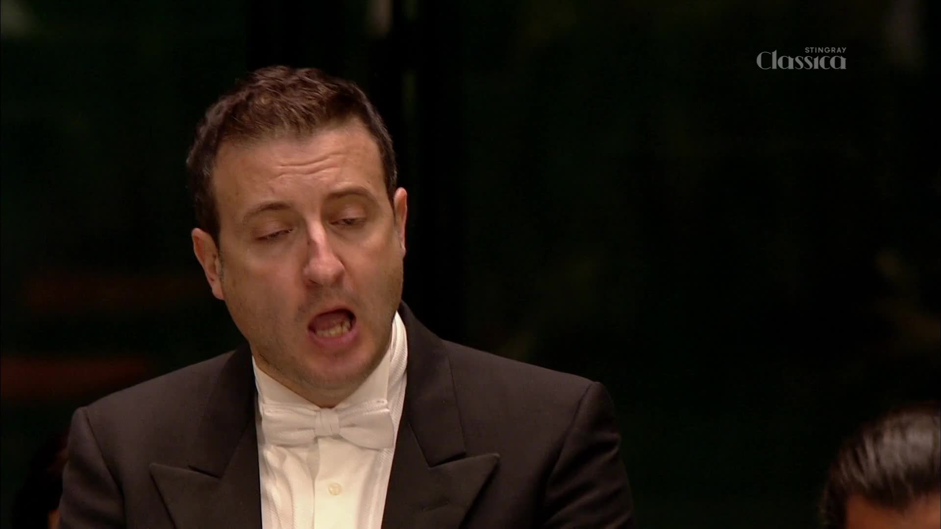 A man in a tuxedo sings with his mouth open, his eyes closed. The Stingray Classica logo appears in the upper right corner. A man in a tuxedo sings with his mouth open, his eyes closed. The Stingray Classica logo appears in the upper right corner.