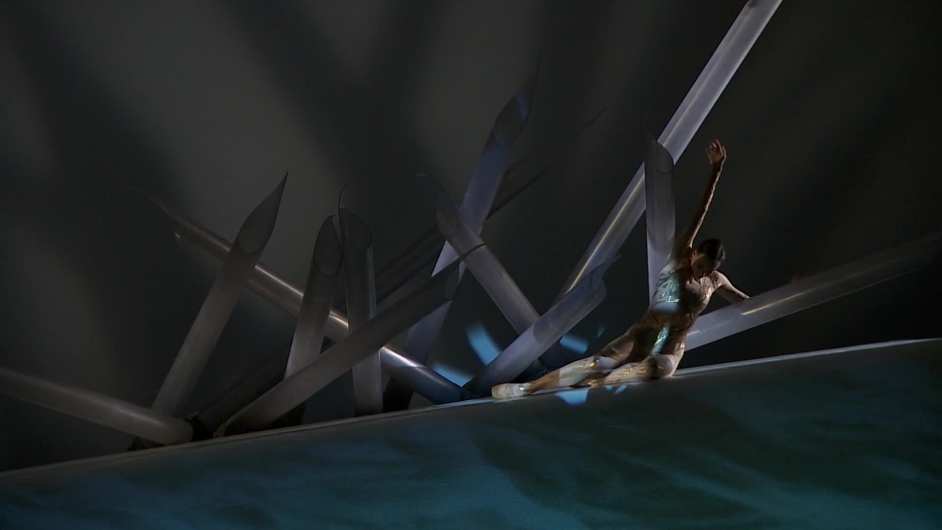 A lone dancer, clad in a shimmering costume, gracefully navigates a stark, angular set. The performance, part of Stingray Classica's Canadian tour, unfolds against a backdrop of sharp, metallic forms.